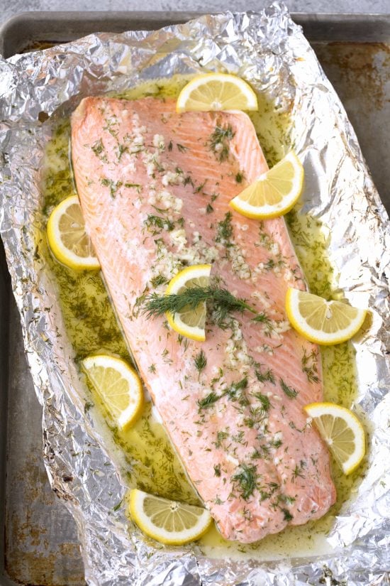 Baked salmon recipe pictured from above that includes lemon, butter, dill, and garlic