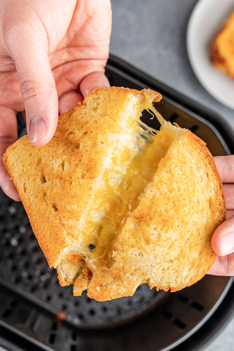 Grilled cheese sandwich being held over an air fryer.