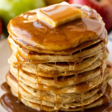 A stack of apple pancakes on a white plate topped with a pad of butter and syrup.