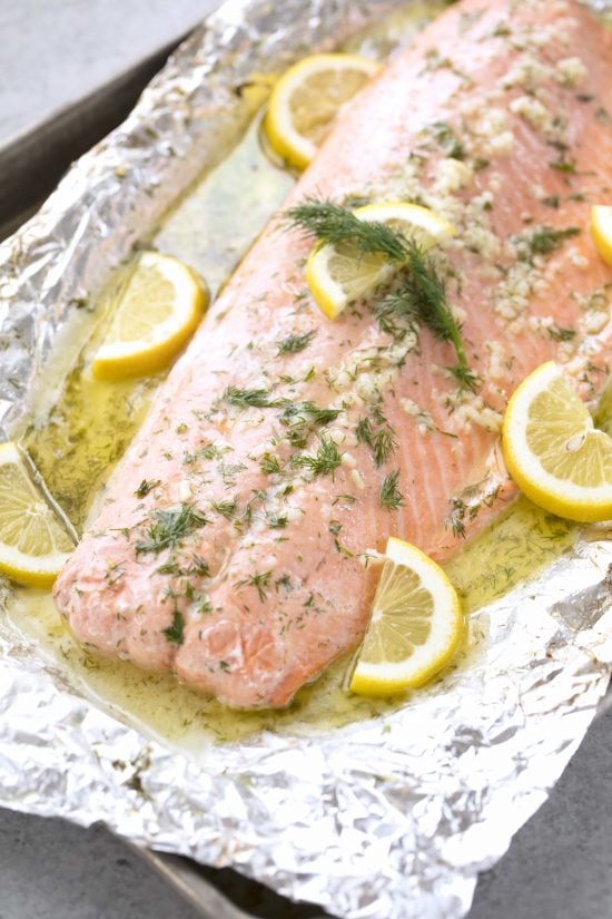 Baked salmon with lemon slices, garlic, and dill sitting in tin foil with all the juices
