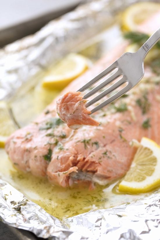 Piece of baked salmon on a fork with large filet of salmon in the background