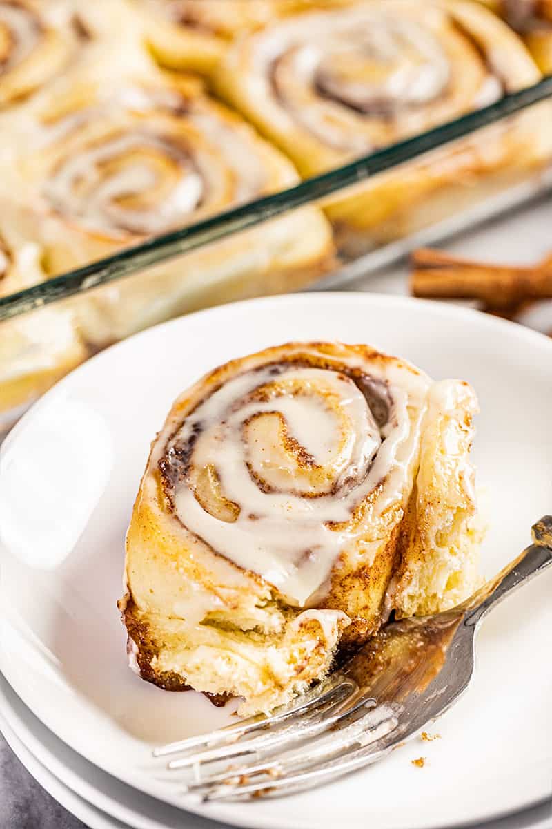 The best homemade cinnamon roll on a white plate with a fork.