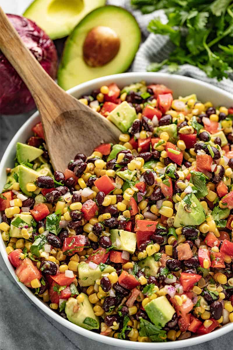 Black Bean and Corn Salad in a white bowl with a wooden spoon in it.