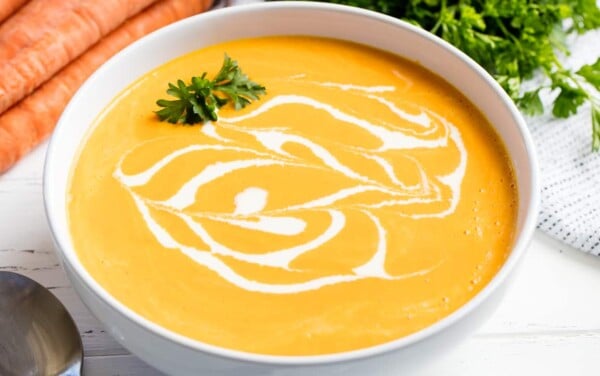 Carrot soup drizzled with cream and garnished with parsley in a white bowl