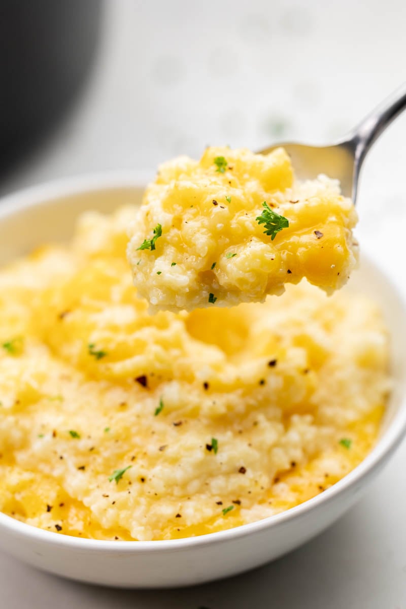 A spoonful of cheesy grits behind held over its bowl.