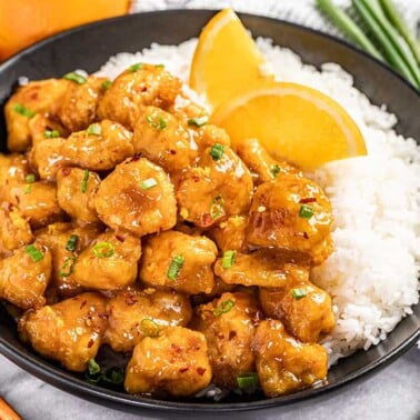 Orange chicken and rice on a black plate.