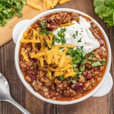 Chili topped with shredded cheese, cilantro and sour cream in a white soup bowl