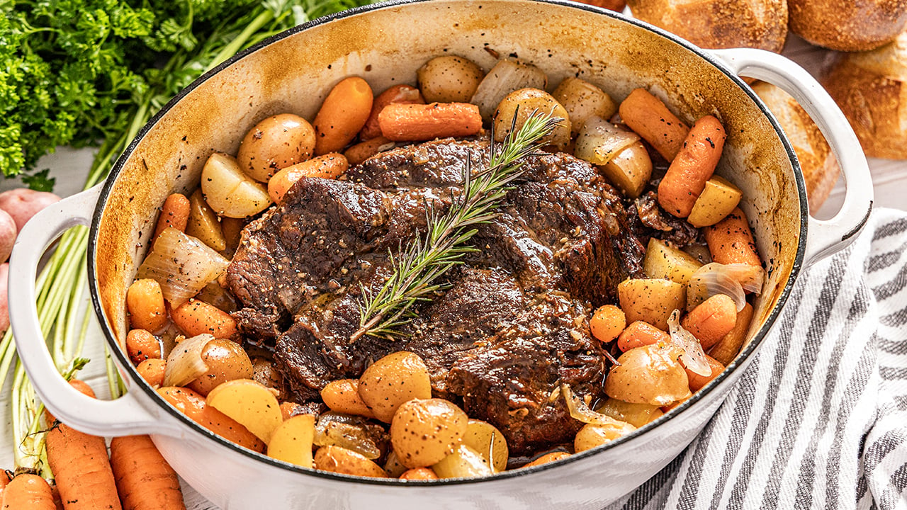 Pot roast surrounded by potatoes and carrots in a large pot.