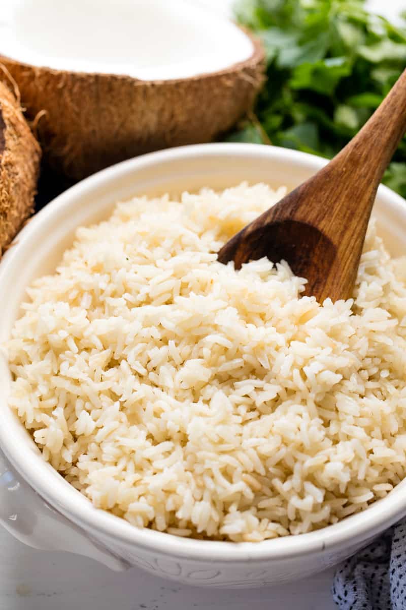 Coconut Rice in a white bowl with a wooden spoon in it.