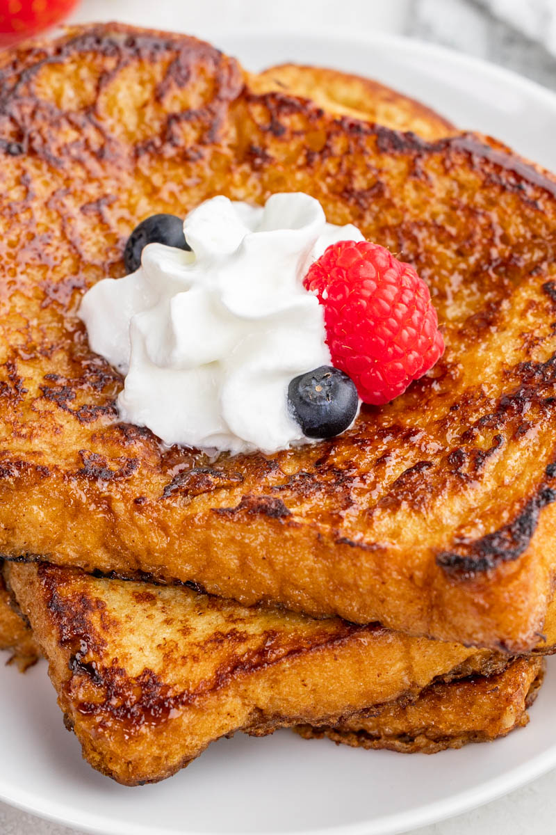 Close up view of Crème brûlée French toast with whipped cream and berries on top.