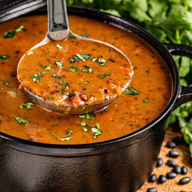 A ladle filled with homemade black bean soup in a large pot.