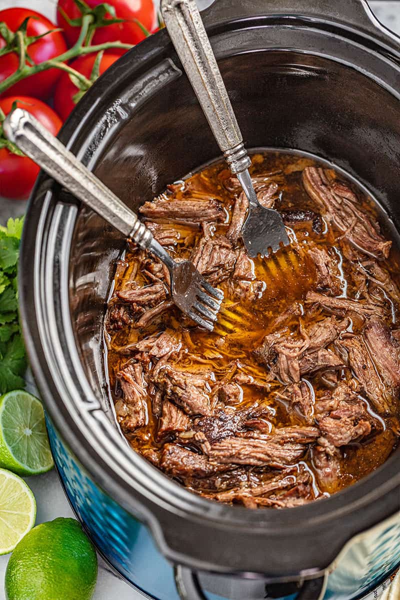 Overhead view looking inside a slow cooker with shredded beef and 2 forks inside.