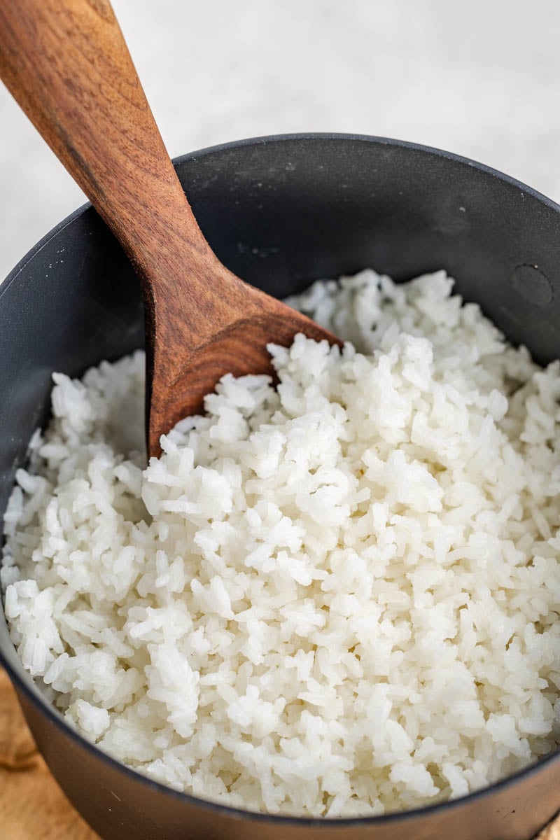 Looking into a pot of fluffy white rice with a wooden spoon.