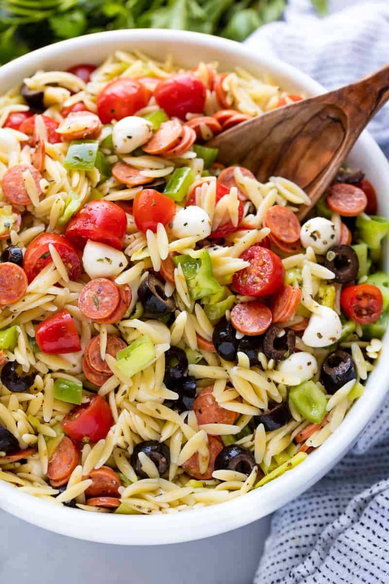 Italian Pasta Salad in a white bowl with a wooden spoon in it.