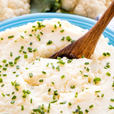 Mashed cauliflower in a blue bowl with a wooden spoon in it.