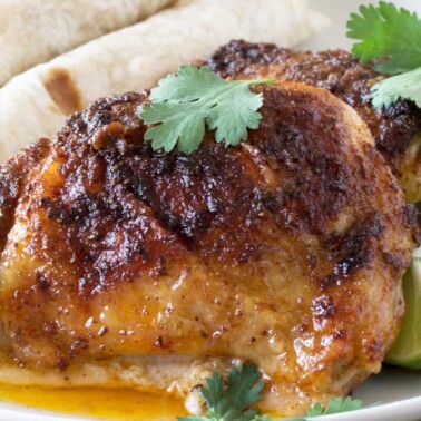 Angled view of Mexican-Spiced Chicken Thighs served up with warm tortillas garnished with lime wedges and parsley.