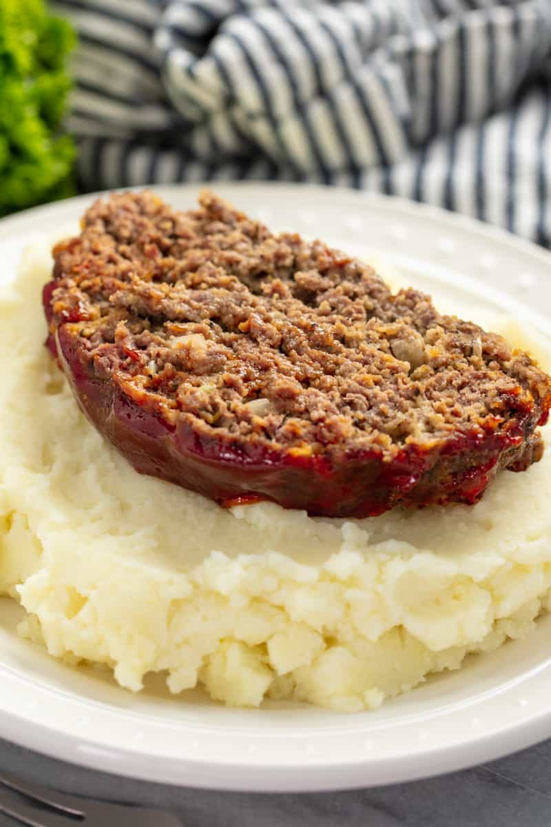 Slice of meatloaf on mashed potatoes all on a white plate.