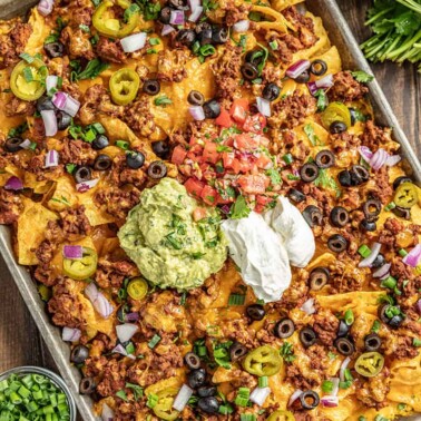 Nachos on a baking sheet with salsa and green onions on the side