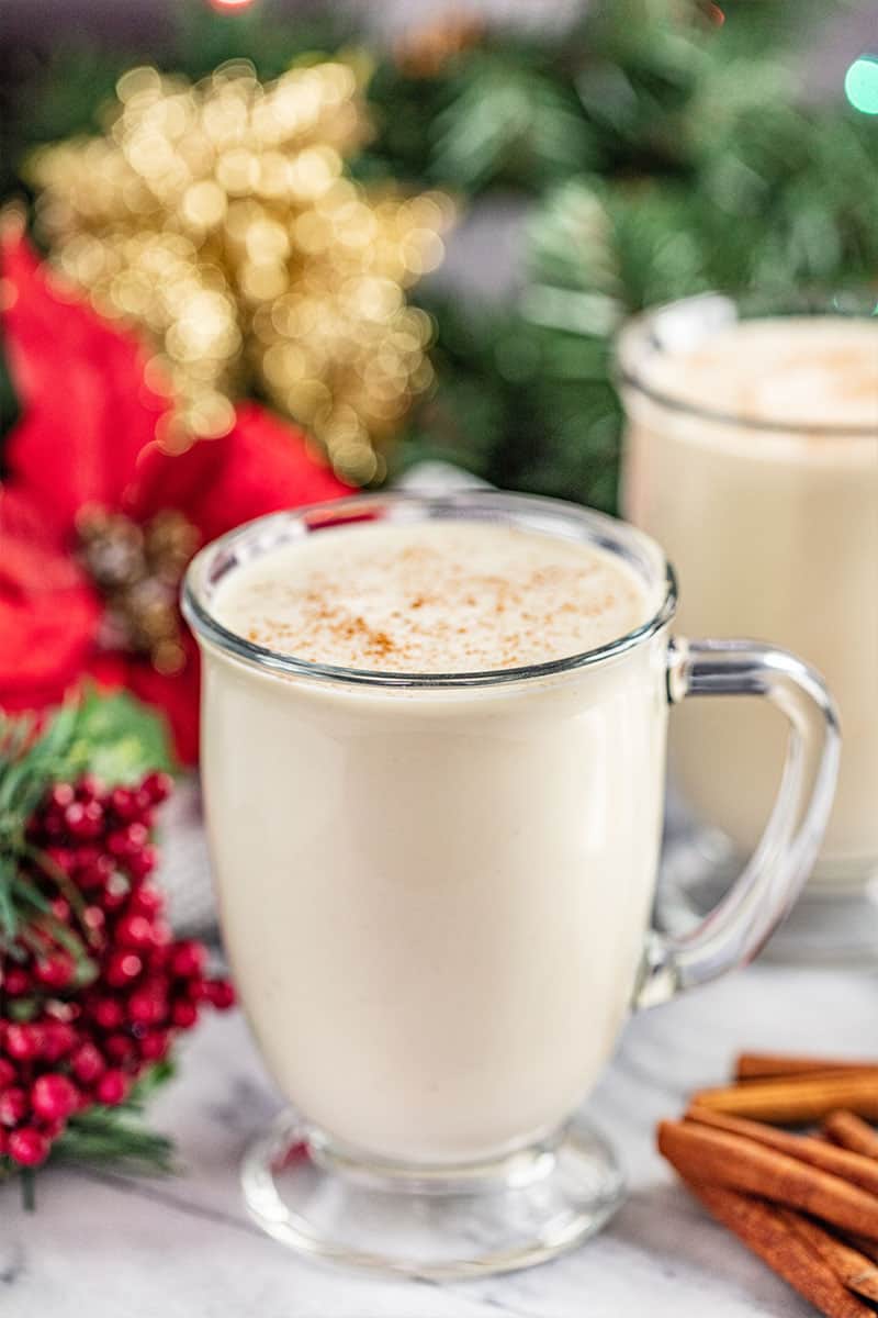 glass mugs filled with eggnog with cinnamon sticks next to the glasses