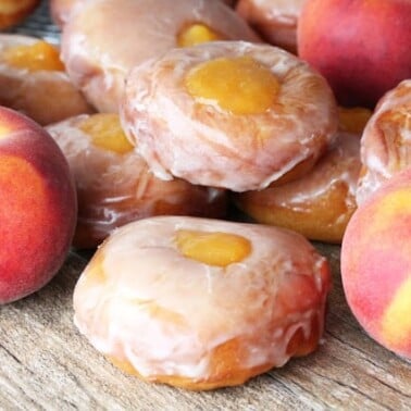 Peach Pie Donuts stacked on a counter with fresh peaches