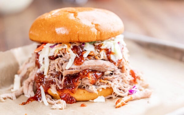 Close up view of a pulled pork sandwich that is overflowing with fillings.