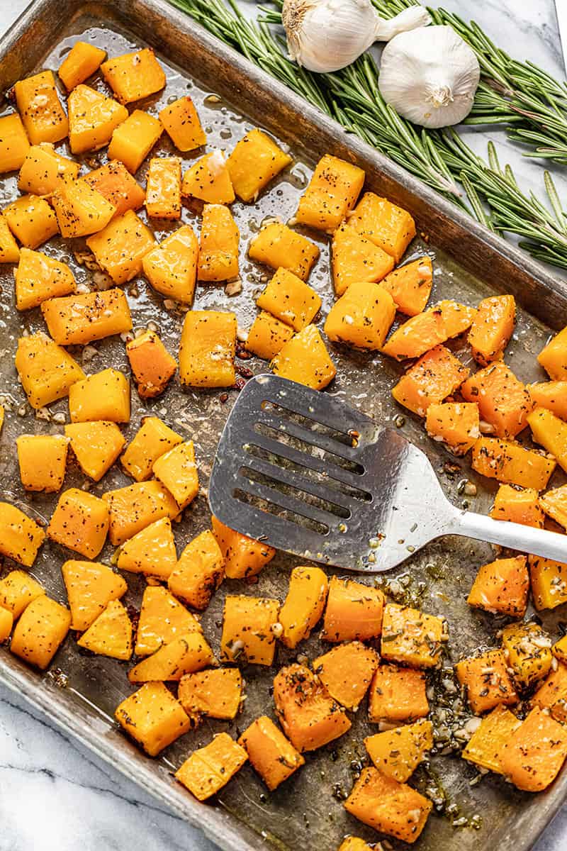 Bird's eye view of butternut squash on a baking sheet with a spatula on it.