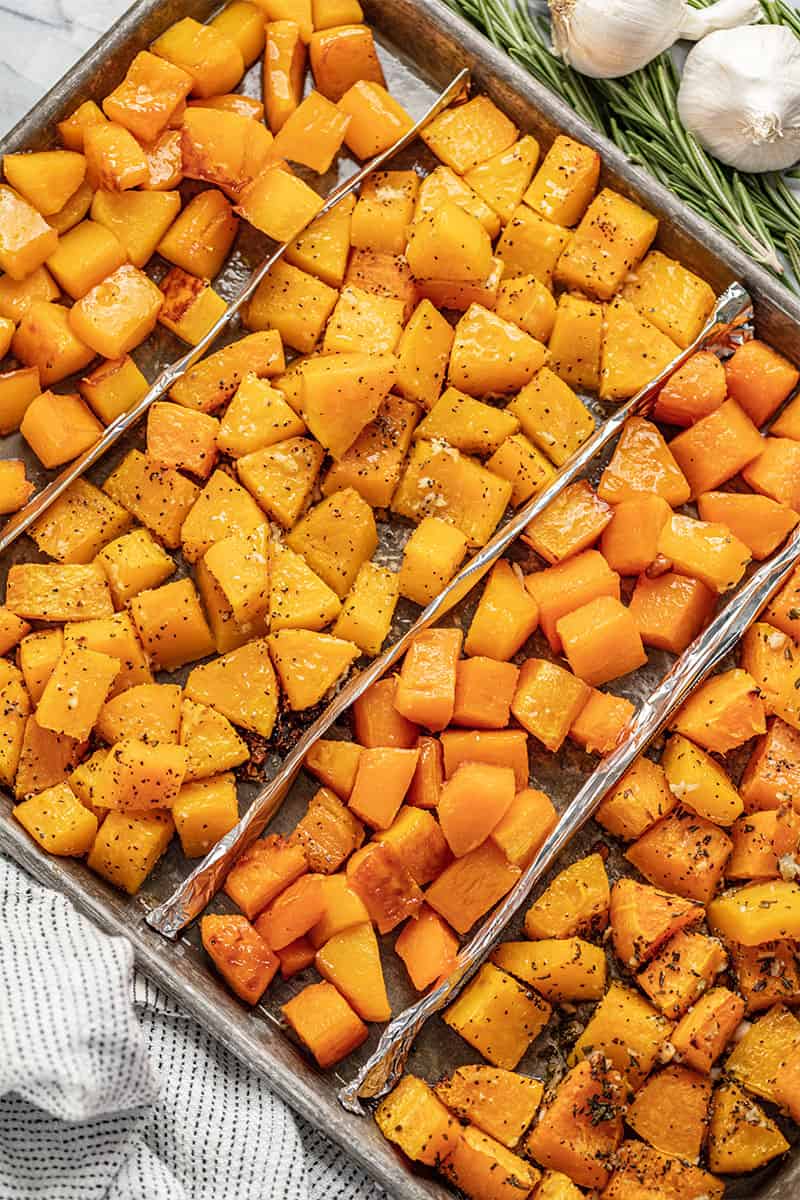 Bird's eye view of four different flavors of Roasted Butternut Squash on a baking sheet.