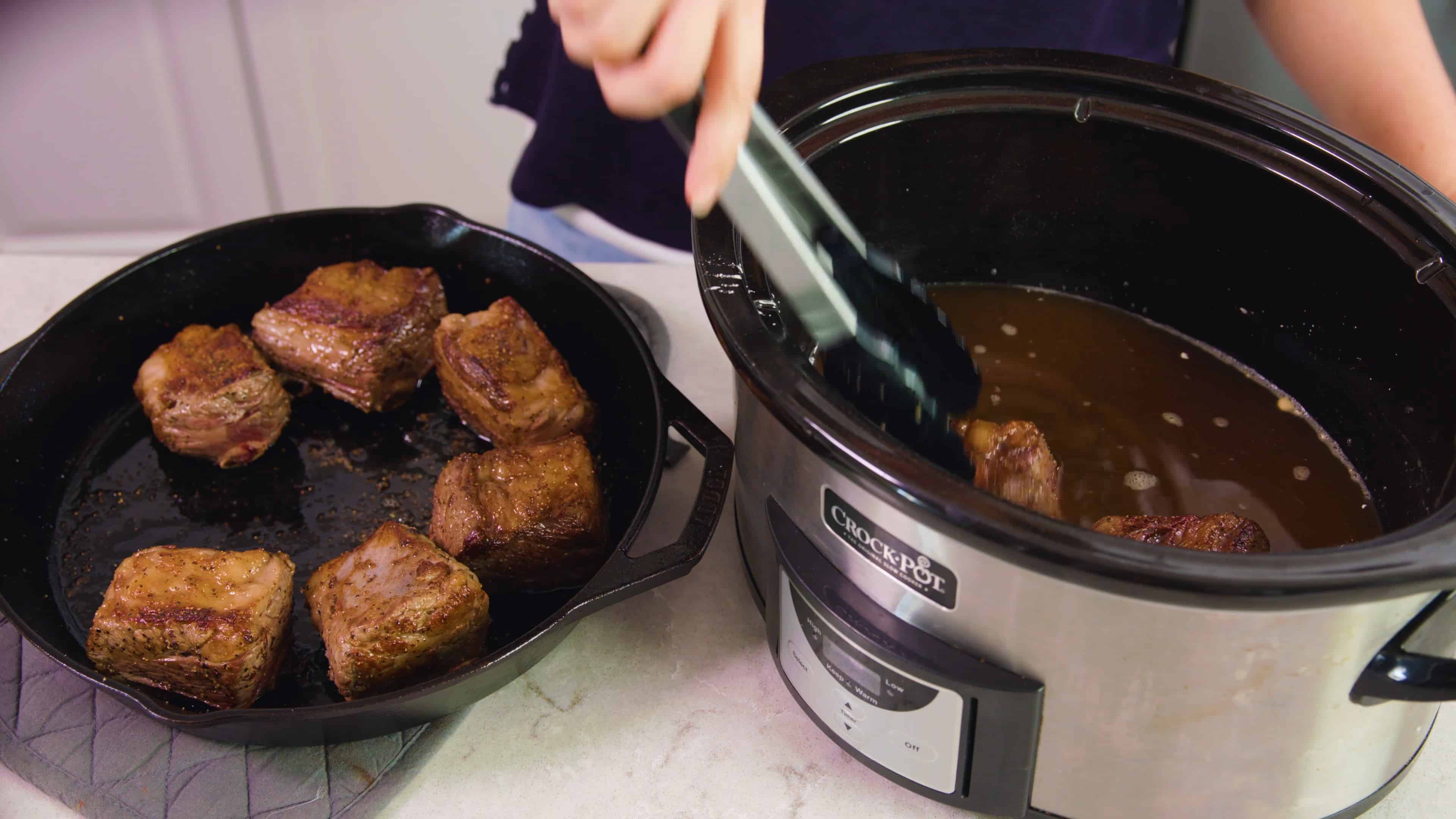 Seared beef short ribs being placed into the slow cooker.