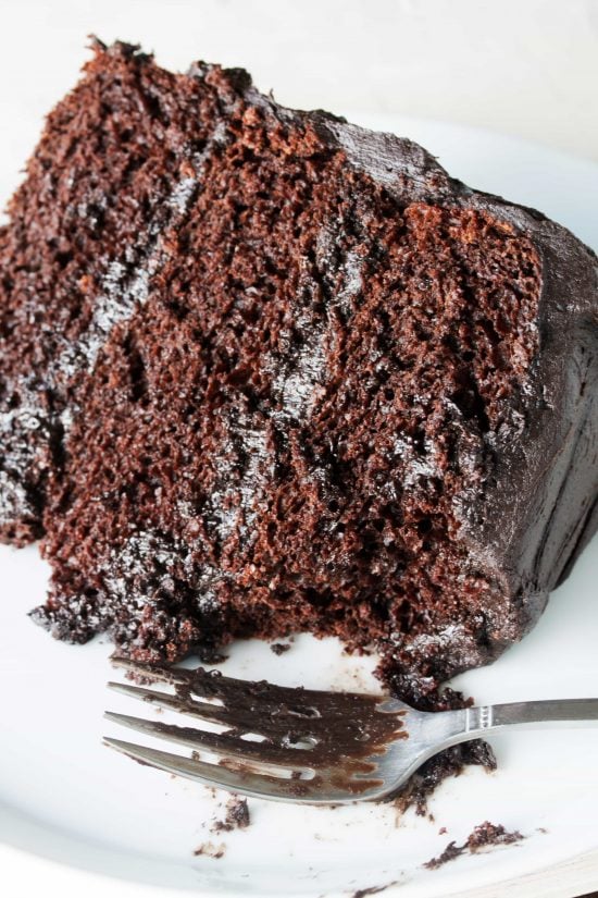 A slice of Moist Chocolate Cake layered with chocolate frosting with a bite taken out with a fork