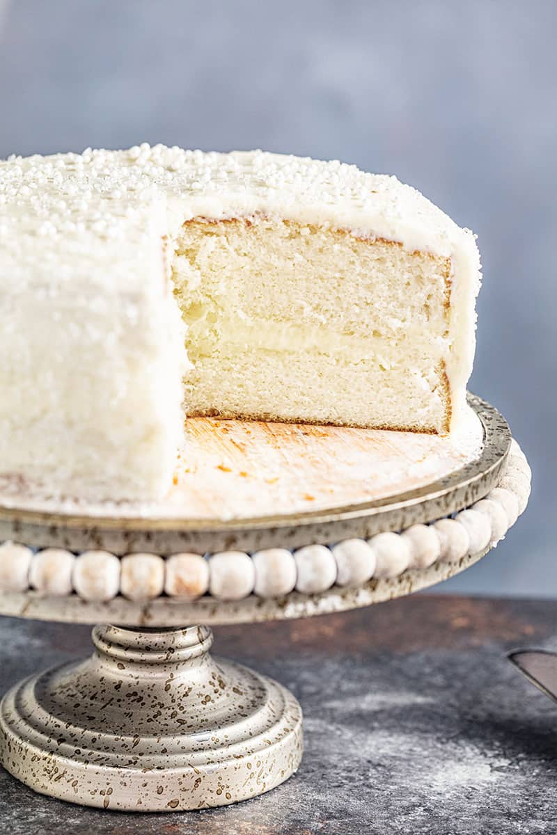 A white cake on a cake stand with one slice removed.