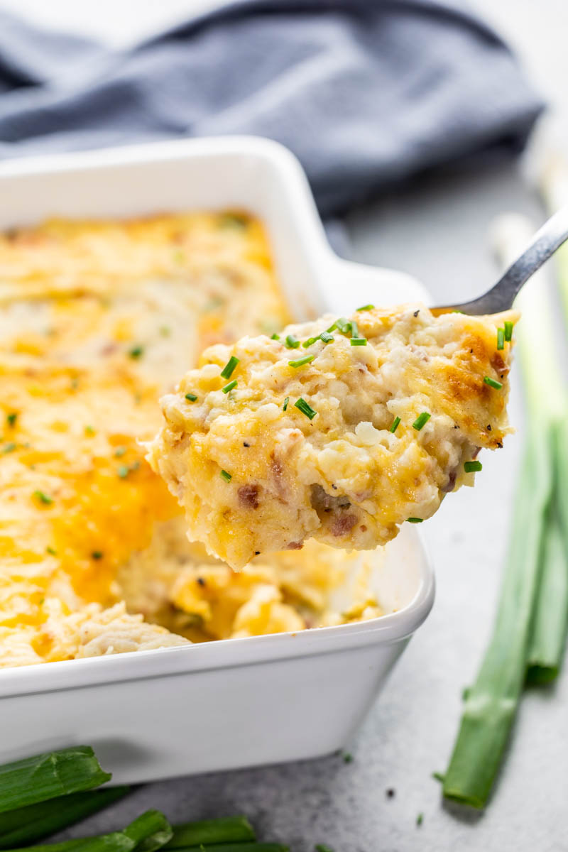 A spoonful being held up filled with twice baked potato casserole.