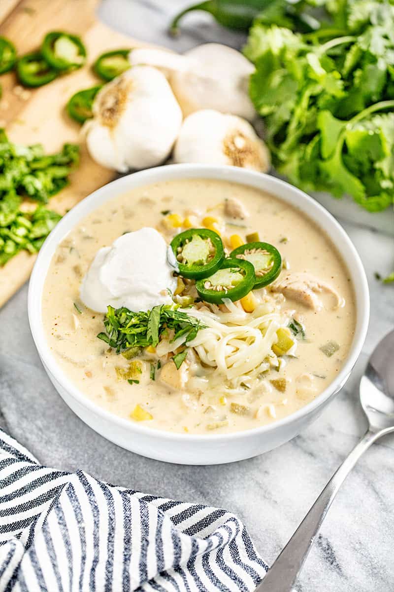 White Chicken Chili topped with cheese jalapeno slices and sourcream all in a white bowl.